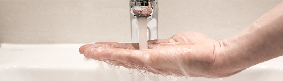 En hand över ett handfat låter vatten från en kran rinna ner i handflatan. 