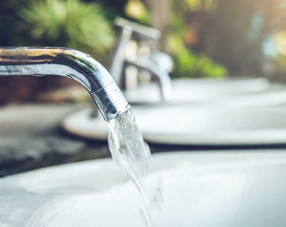 Vatten rinner från en vattenkran ner i ett handfat.