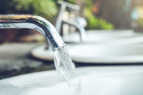 Vatten rinner från en vattenkran ner i ett handfat.