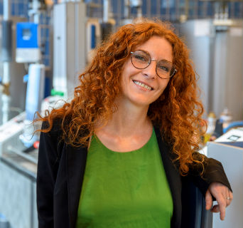 Giulia Botta, Global Business Development Manager for Energy Transition, with curly red hair and glasses smiling and leaning against industrial equipment in a professional setting