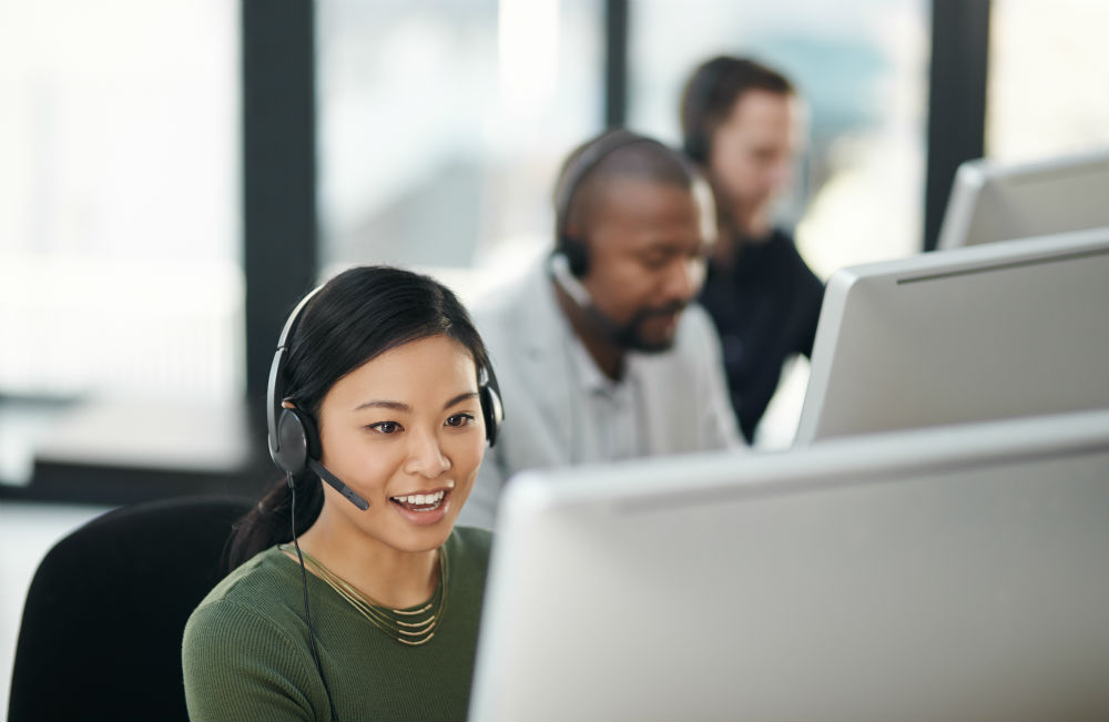 Tre personer med headset sitter i rad framför varsin datorskärm.
