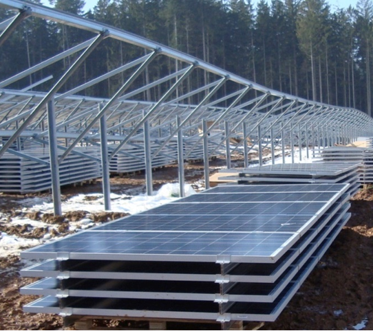 Paneles solares apilados en un bosque, listos para ser instalados en estructuras metálicas.
