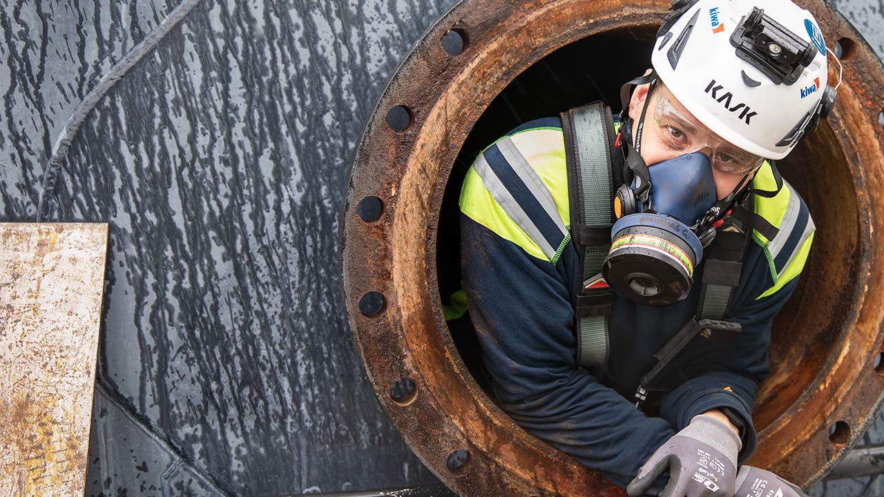 Man med gasmask tittar ut från arbete i slutet och trångt utrymme.