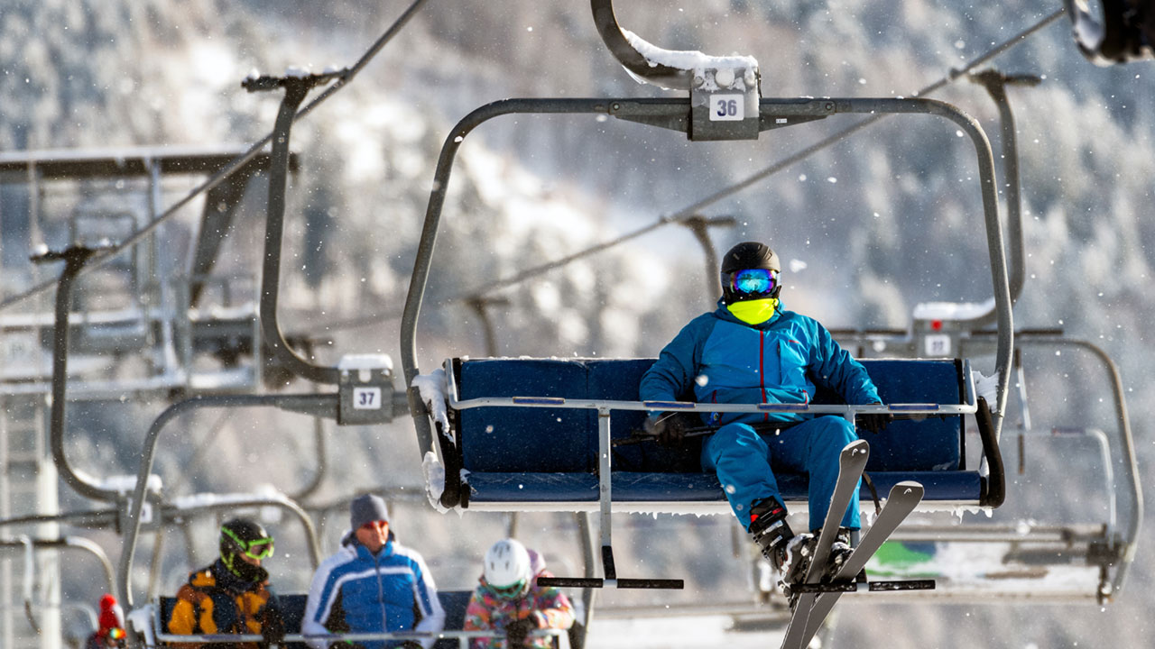 En ensam skidåkare åker en korglift uppför slalombacken, det snöar. 